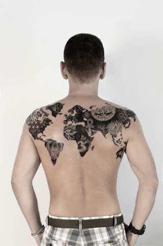 Back view of a man with a world map tattoo across his back, filled with spiritual and ethnic symbols like the lotus, Eye of Horus, mandalas and tribal patterns. Tattoo by French artist Delphine Cencig, based in Montenegro.