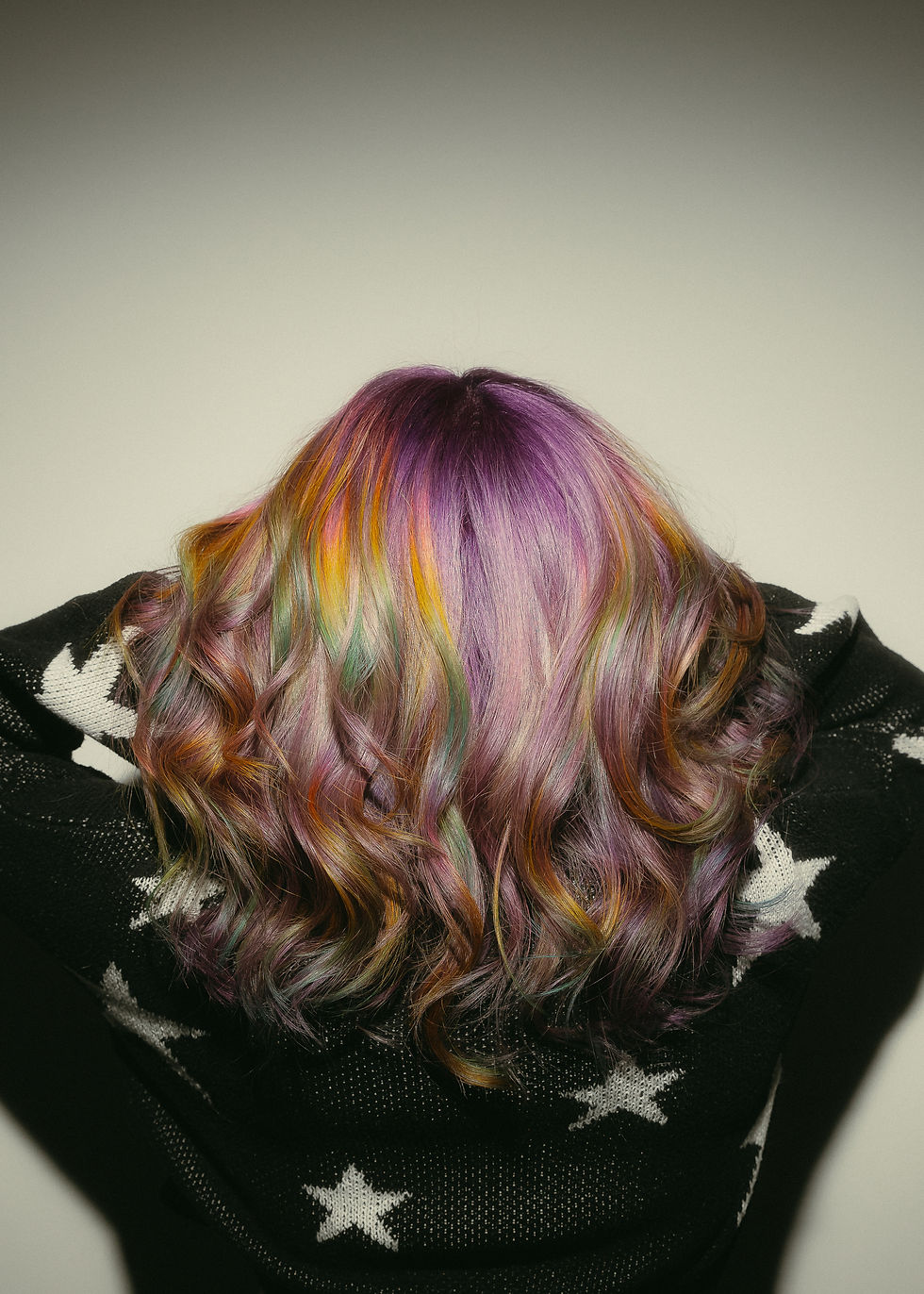 photo of colorful rainbow hair styled in uniform waves. base of hair is a silver purple color and there are pops of holographic rainbows throughout.