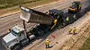 AI pedestrian detection for dump trucks — aerial view of dump truck at road construction site with ground crew and flaggers on foot nearby.