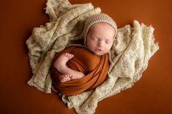 wrapped posed newborn baby boy in Murfreesboro TN on burnt orange backdrop and beige textured blanke