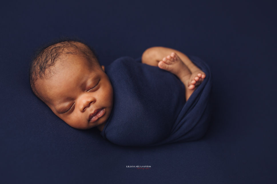 Newborn baby boy photographed in the studio in North Wales. Posed baby in a blue swaddle wrap.