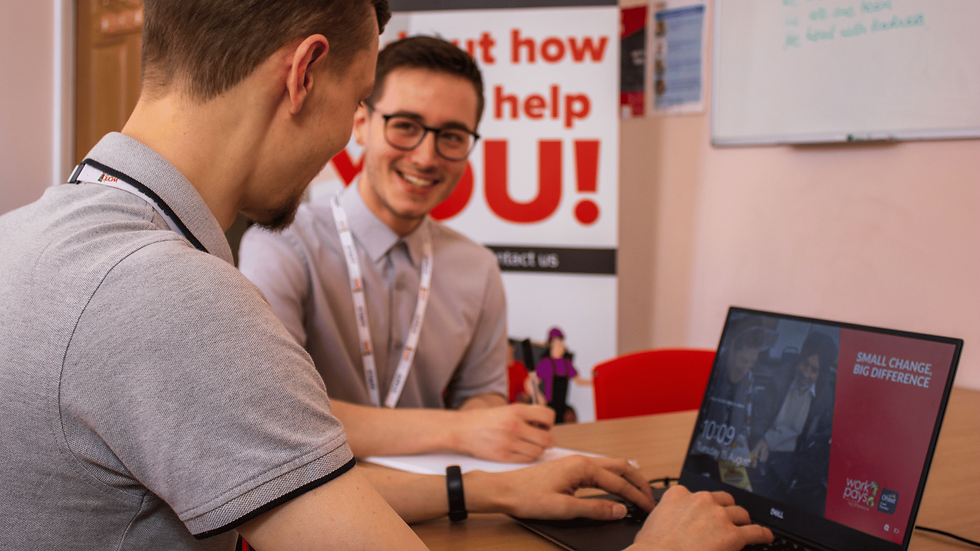 Two men smile at a booth while using a laptop; a poster behind reads Small change, big difference.
