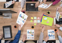Arms of random people exchanging documents at a conference room table conveying a meeting is taking place.