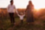 Family walks hand-in-hand in a sunlit field, with a child in the center. Warm sunset tones create a serene, joyful atmosphere.