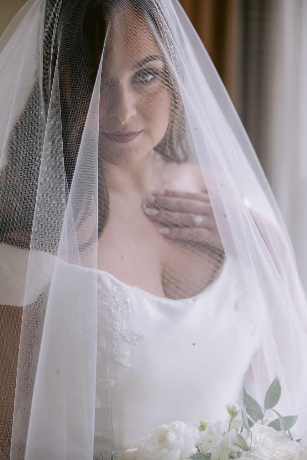 Bride adjusting veil while groom looks on smiling