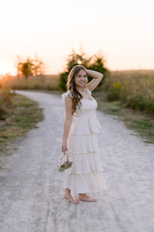 Senior girl walking through tall grasses, wearing a long flowy dress, looking at the camera.