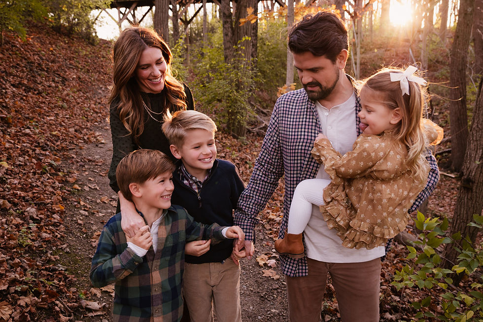 A family walking through golden leaves during a fall photo session at Flat Fork Creek Park in Fishers, Indiana.