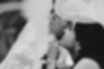 Bride and groom embrace under veil, sharing an intimate, joyful moment. Black and white, soft focus on faces, highlighting the bride's earring.