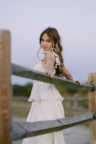 Senior girl walking on a gravel path lined with wildflowers, glancing back over her shoulder.