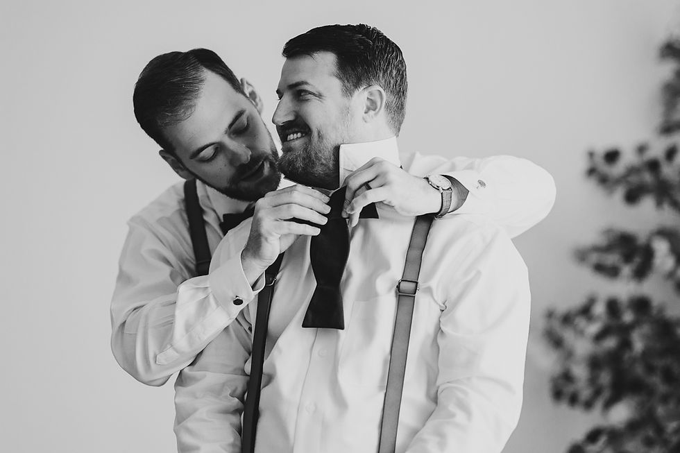 Candid moment of two grooms helping each other get ready on their wedding day, captured in authentic documentary style wedding photography in Indianapolis.