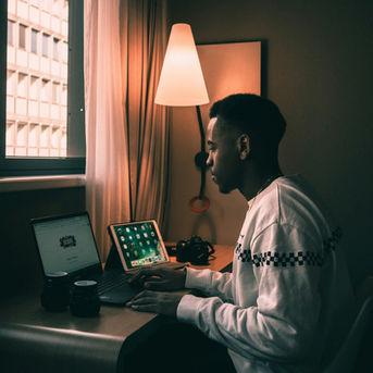Guy on 2 devices working at a desk with a lamp