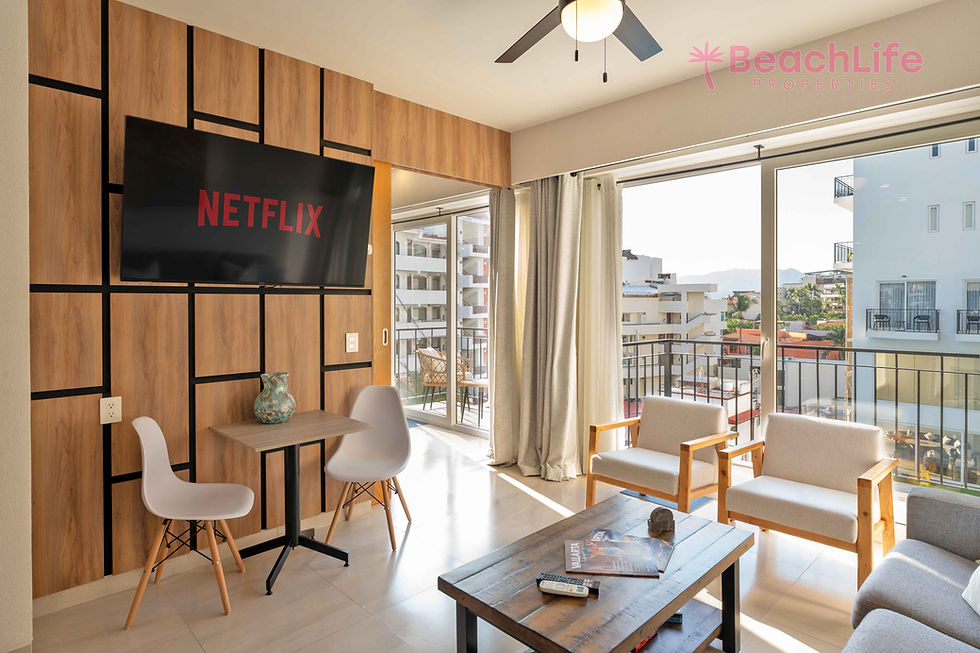 Modern living room with balcony views, Netflix on wood-paneled TV, two chairs at a small table, ceiling fan, and magazines on a coffee table.