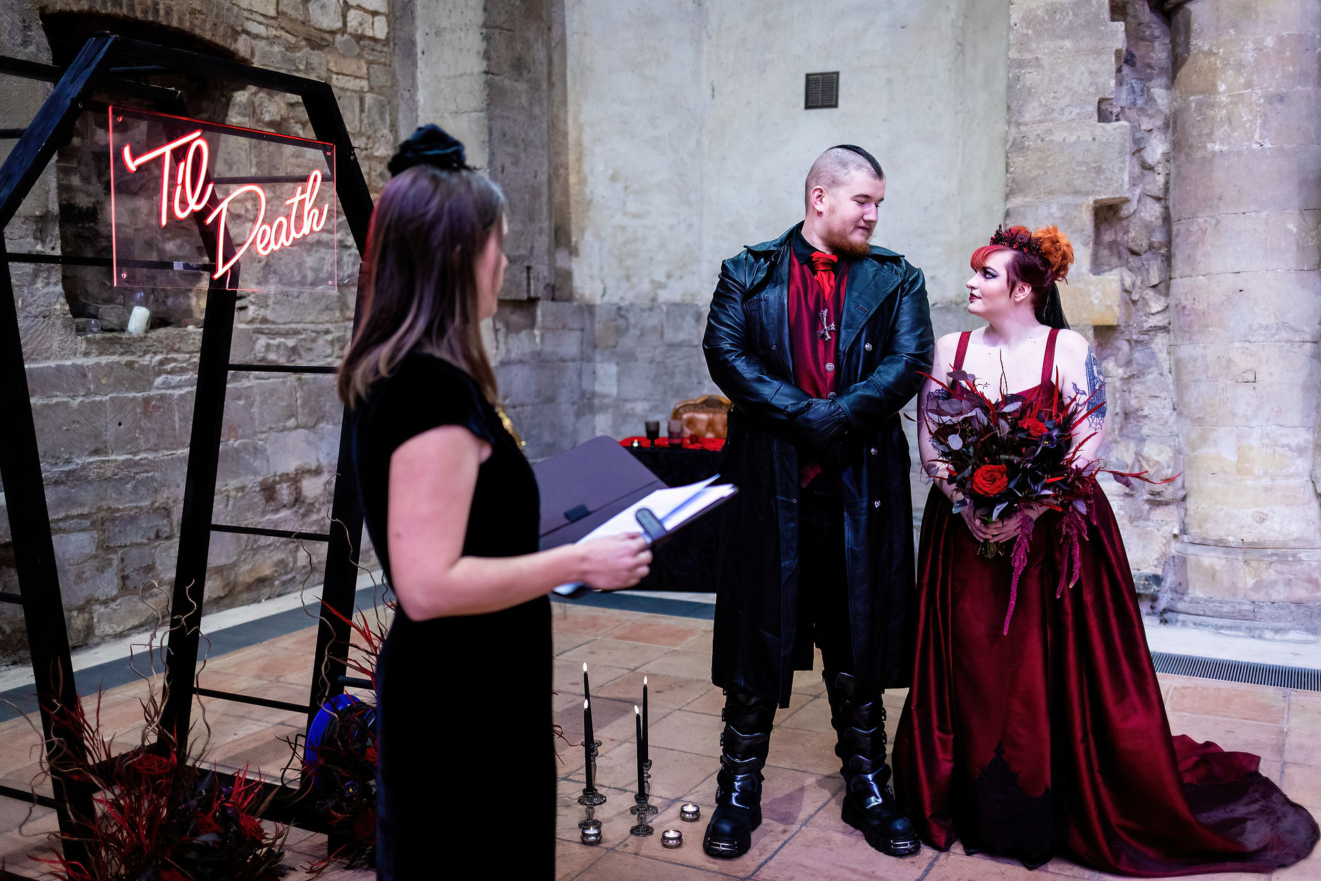 an alternative couple wearing black and red exchange loving glances at the alter
