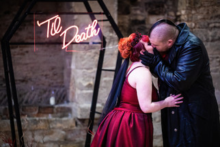 gothic couple share a kiss in front of a coffin shaped alter