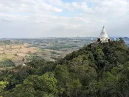 A lone white pagoda crowns a steep hill, offering 360-degree views of the rural plains.