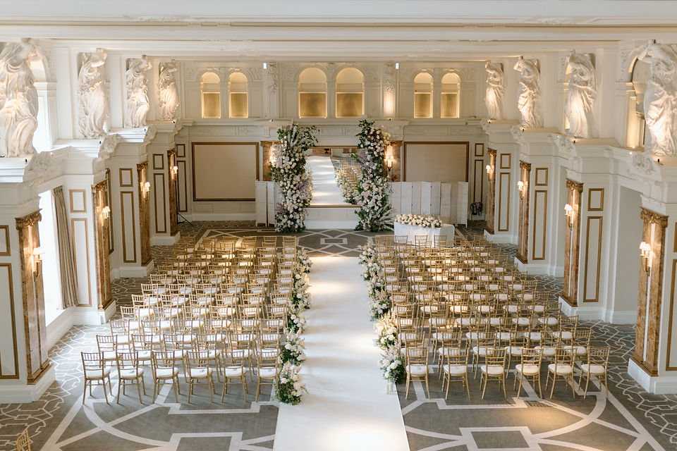 A luxurious wedding reception in the grand ballroom of the Kimpton Fitzroy Hotel in London, featuring elegant chandeliers, opulent décor, and beautifully arranged tables surrounded by guests in formal attire, exquisitely designed and styled by a luxury UK wedding planner.