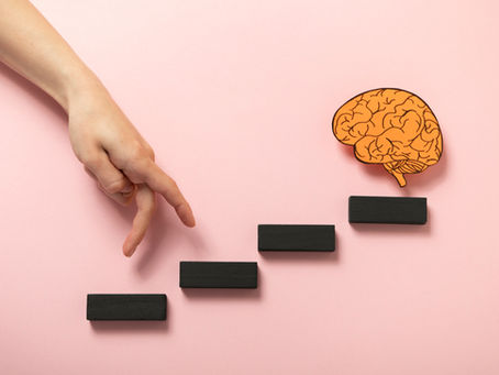 Main en marche sur pavés noirs formant des marches, vers un cerveau dessiné, sur fond rose. Symbolisme de l'apprentissage et de la mentalité de croissance.