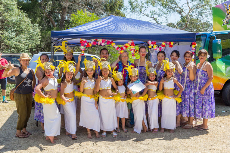 Children's cultural dance troupe in yellow and white costumes under a marquee tent