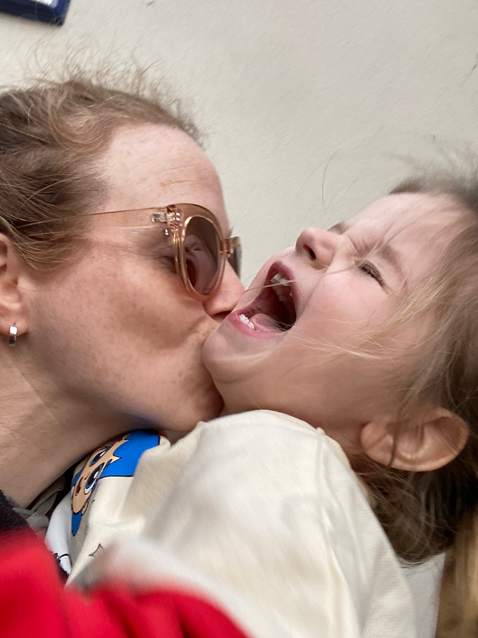Mom Kissing her toddler and the toddler is head back laughing