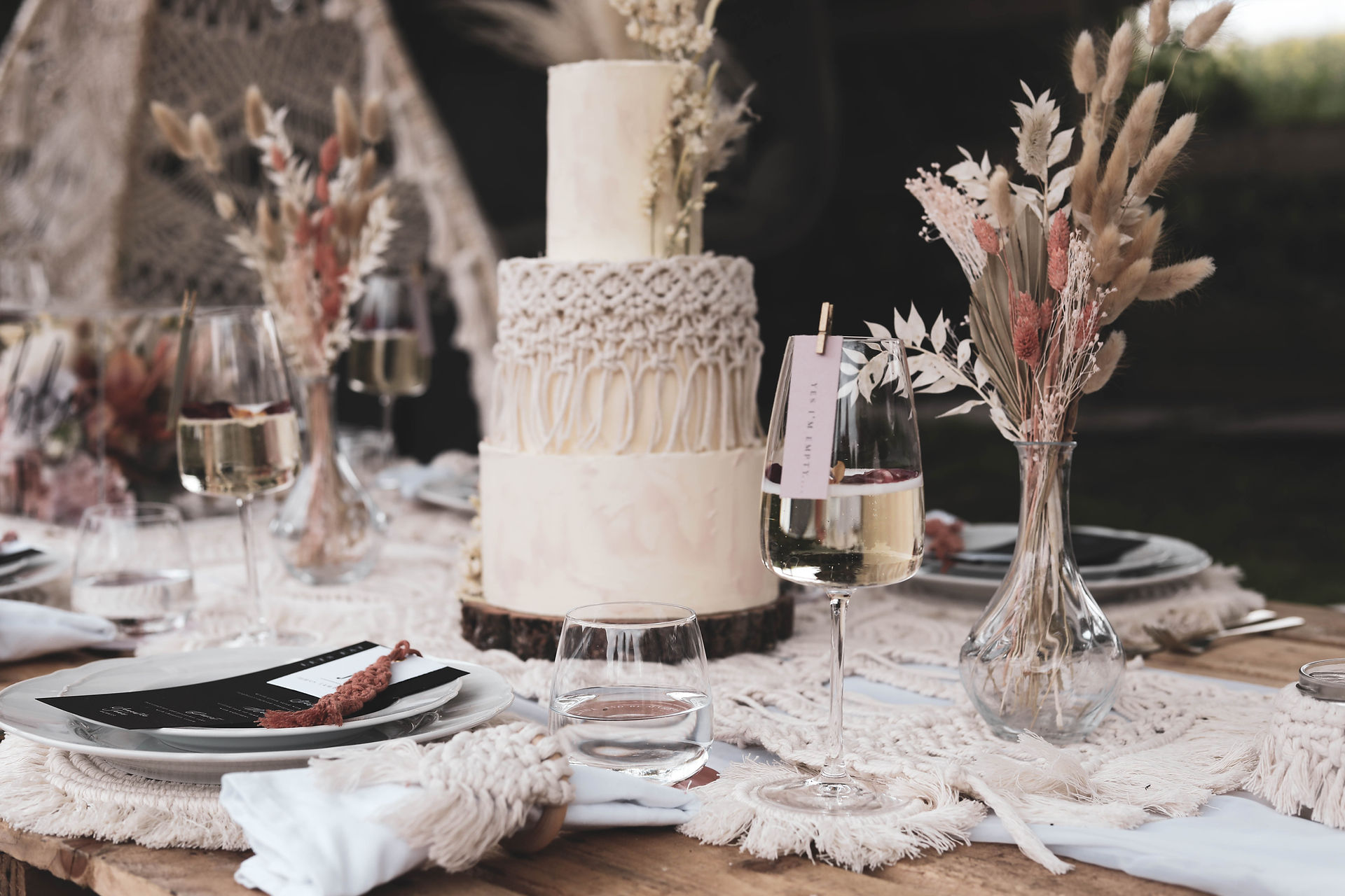 Boho decor adorns this wedding breakfast table; a three tier cake with dried flowers and macramé table runners