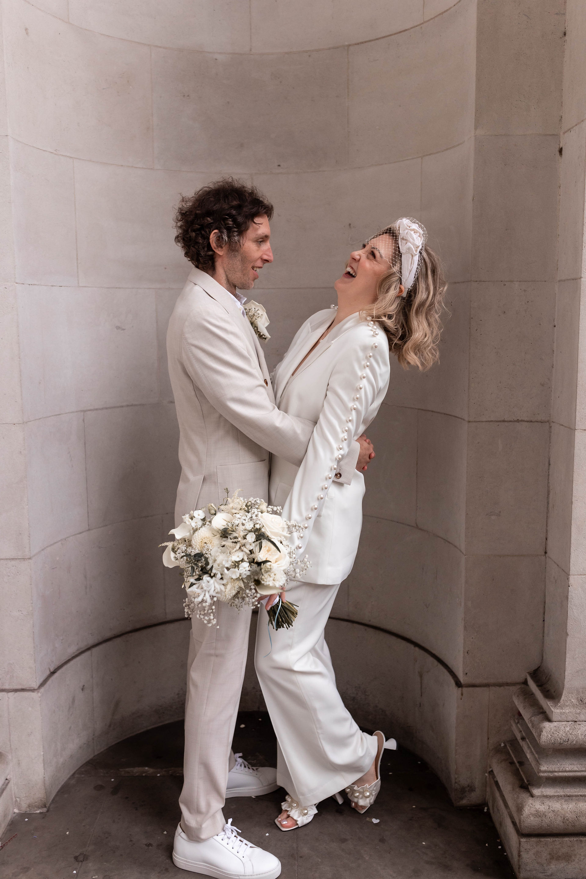 The bride and groom laugh in the arches at the iconic Old Marylebone Town Hall, London