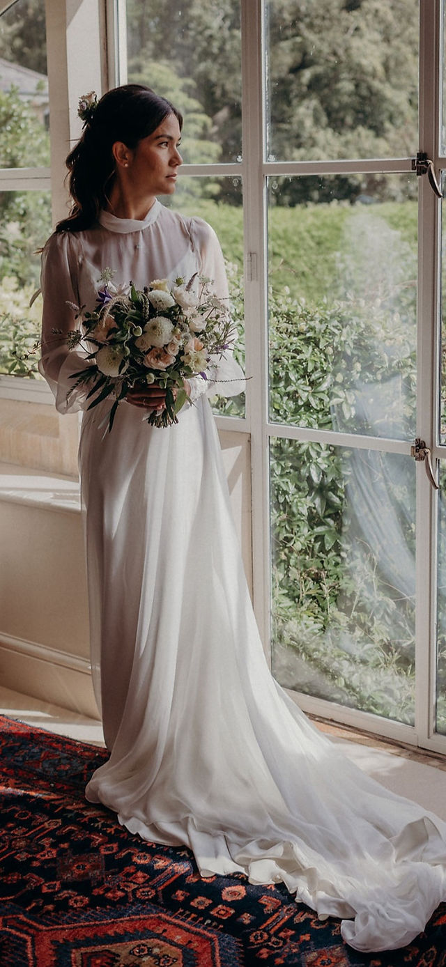 Bride in white dress holding flowers near window, The Magic of Bespoke Wedding Dresses.
