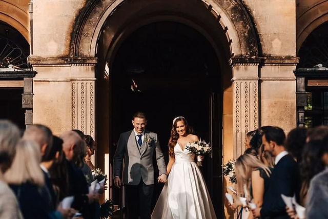 Newlyweds exiting church, holding hands, with guests, The Magic of Bespoke Wedding Dresses