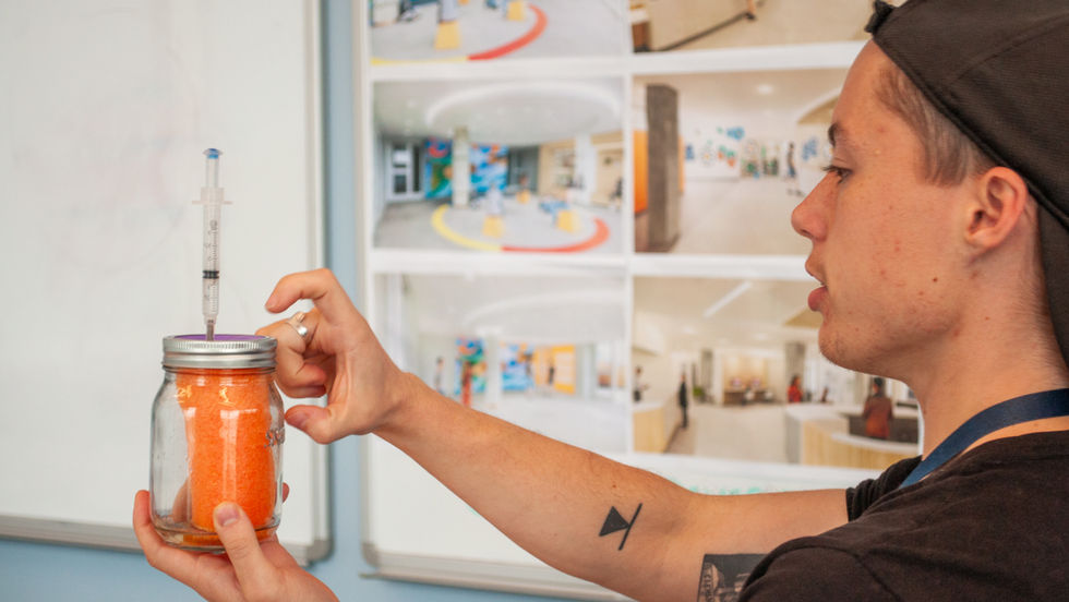 A person using a syringe on a mason jar full of orange sponge.