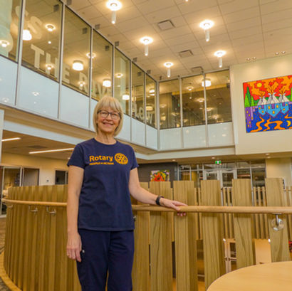 A woman wearing a shirt that says "Rotary: People of Action" stands in a well-lit, modern building.