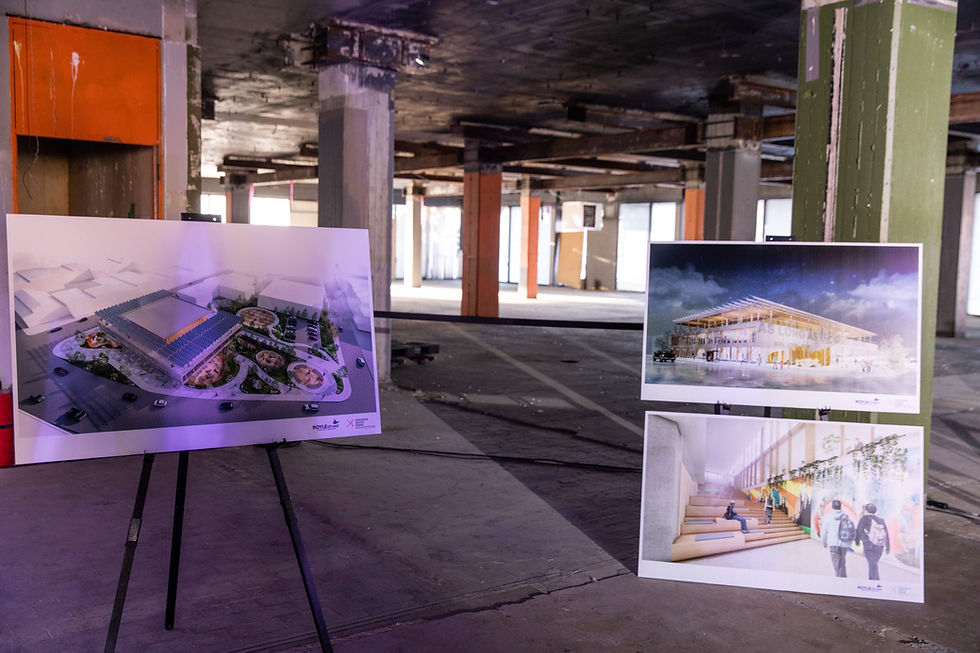 Display boards showing architectural designs stand on easels in an empty, dimly lit building with exposed columns and a concrete floor.