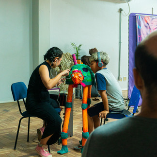 Uma atriz apresenta uma cena de teatro lambe-lambe para um menino. A cena acontece dentro de uma tartaruga verde com longas pernas laranjas.