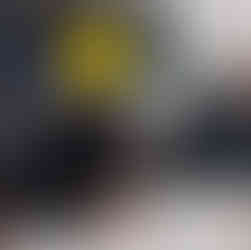 Menino segura a cabeça de um mamulengo, na classe está a massa de papel machê.