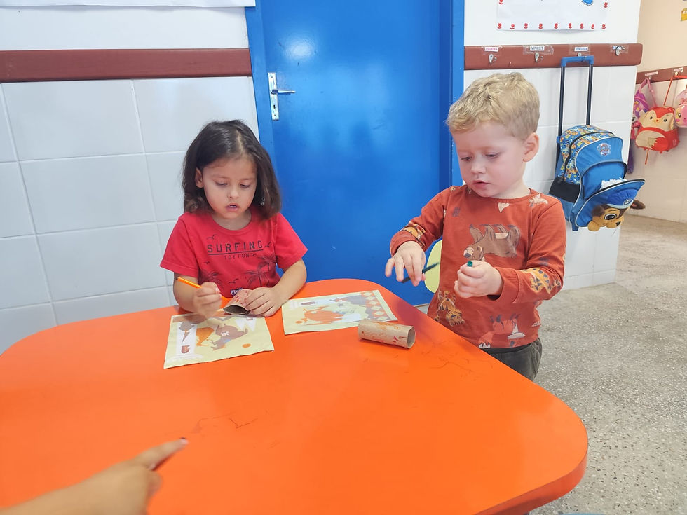 Dois alunos brincando com seus bonecos de rolinho de papel sobre uma mesa laranja.