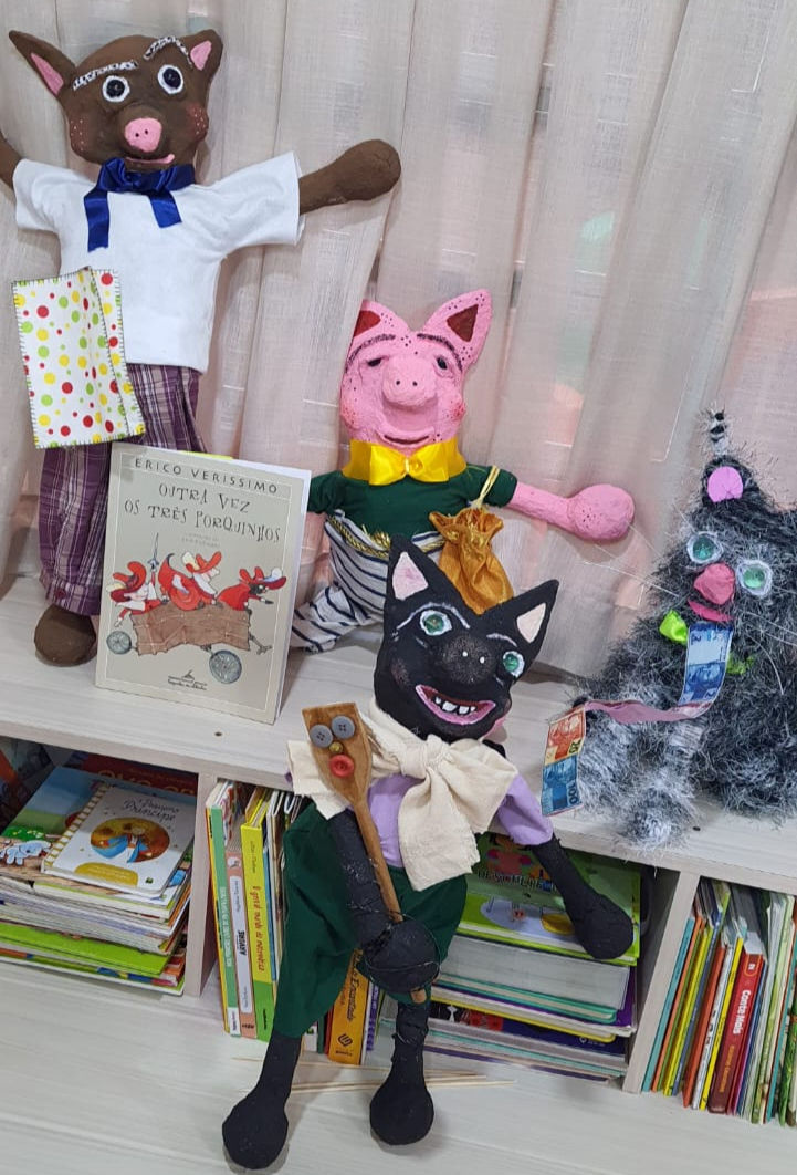 Bonecos de porquinhos e um lobo em uma estante com livros.