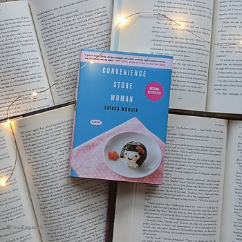 On top of four open books is a smaller book, Convenience Store Women with yellow fairy lights on top of the image.