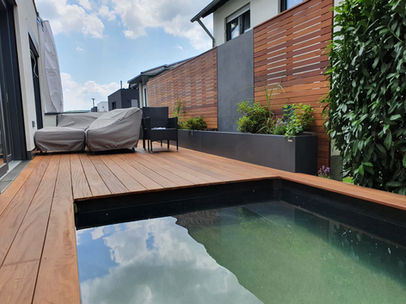 Pool im Hausgarten mit Hartholz-Terrasse und Rhombusleisten als Sichtschutz. Wasserwand mit Natursteinplatte vom Gartenbau Helmich