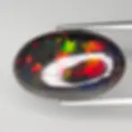 Opale fumée 5.44ct, jeu de couleurs feu intense rouge et vert, cabochon ovale allongé sur fond blanc.