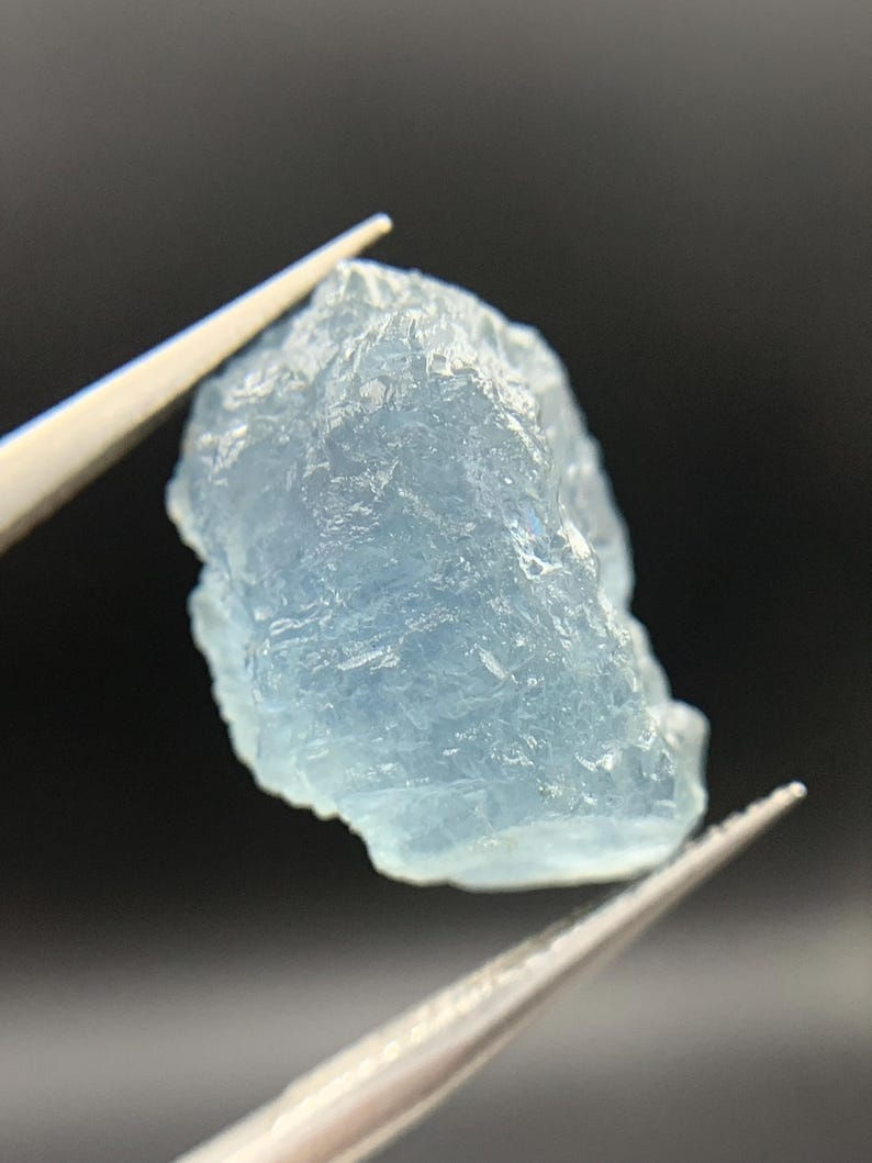 Thumbnail: Cristal d'afghanite brute de Badakhshan montrant une fluorescence orange vive sous lumière UV et un habitus naturel bleu-gris