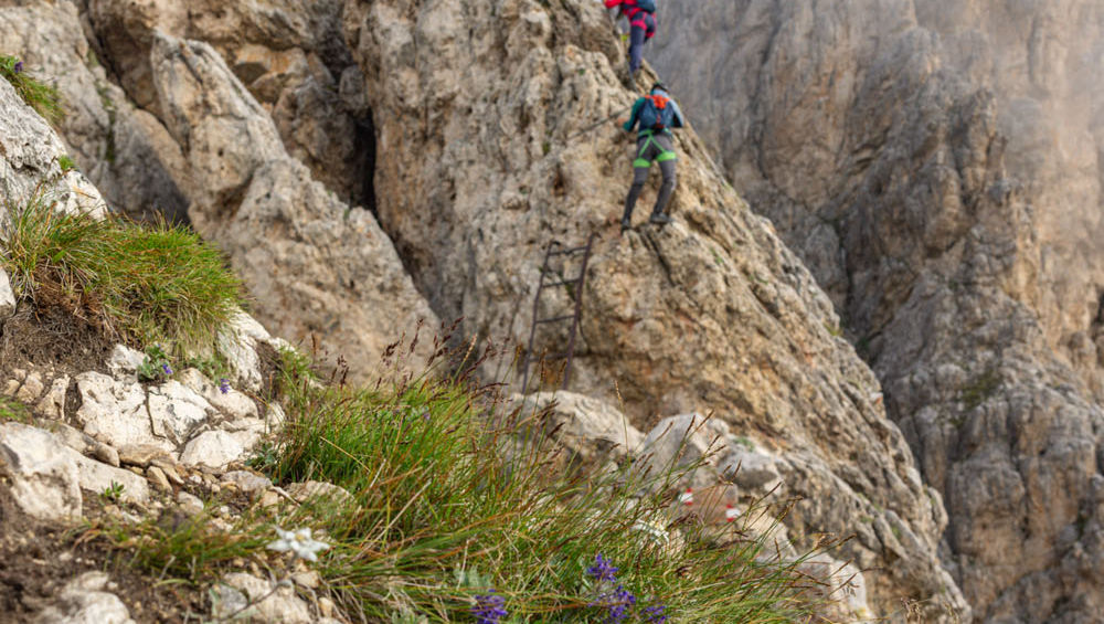 Climbers traversing exposed rocky via ferrata section in the Dolomites secured to steel cable