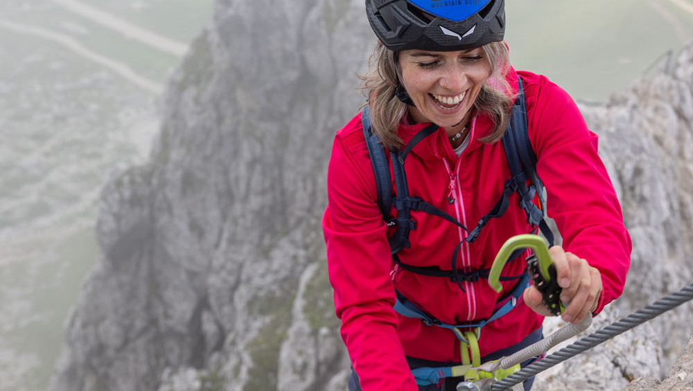 Woman climbing steep via ferrata wall in the Dolomites using steel cable and safety gear on vertical rock