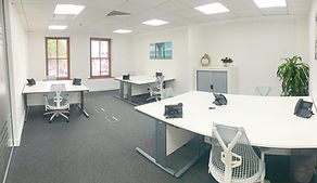 A clean, white, fully furnished private office space with desks, chairs and natural light from windows