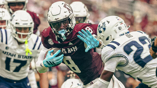 Football player in maroon jersey runs with ball, fending off opponent in white jersey. Action scene on field; teammates in background.