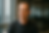 Mark Zuckerberg. Man in a gray shirt sits indoors, looking thoughtful. Background has a blurred office setting with large windows and neutral tones.