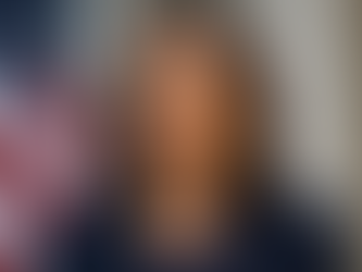Kamala Harris. A woman in a navy blazer and pearl necklace stands confidently with an American flag in the background.
