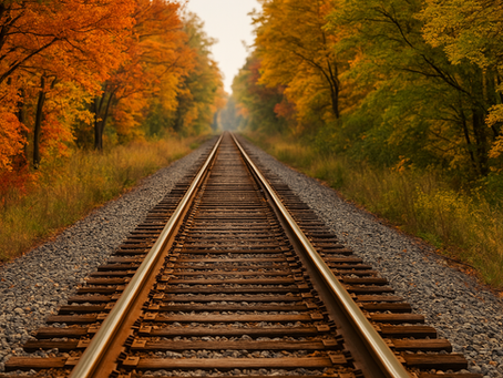 Railroad tracks stretch into the distance, flanked by vibrant autumn trees with orange and yellow leaves, evoking a serene, timeless mood.