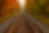 Railroad tracks stretch into the distance, flanked by vibrant autumn trees with orange and yellow leaves, evoking a serene, timeless mood.