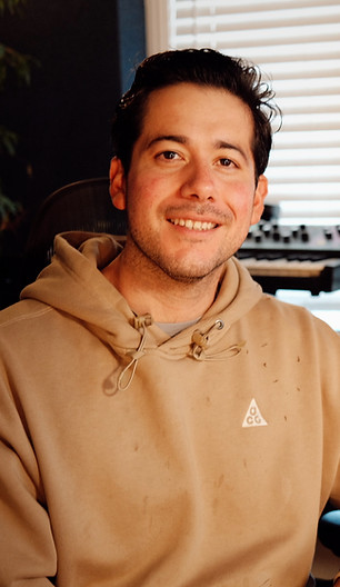 Music producer sitting in a studio surrounded by synthesizers and keyboards
