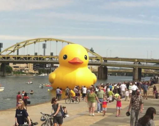Extremely large yellow rubber duck floating in the river in front of a classic Pittsburgh yellow bridge