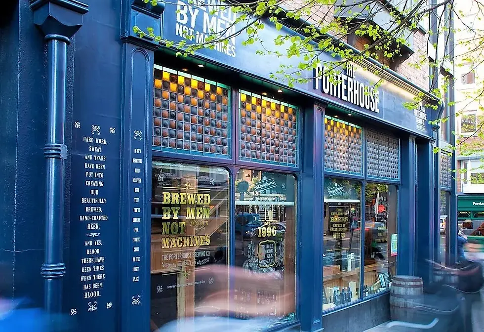 Pub exterior with blue facade, textured glass, and text: "BREWED BY MEN, NOT MACHINES." Warm lighting, trees above, city street scene.