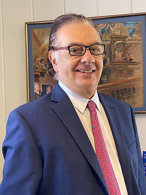 Greg Denaro's headshot. Blue suit jacket, white shirt, and a red tie